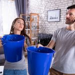 Couple Using Bucket For Collecting Water Leakage From Ceiling